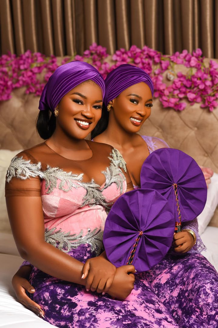 Two ladies in coordinated pink and purple attire with hand fans